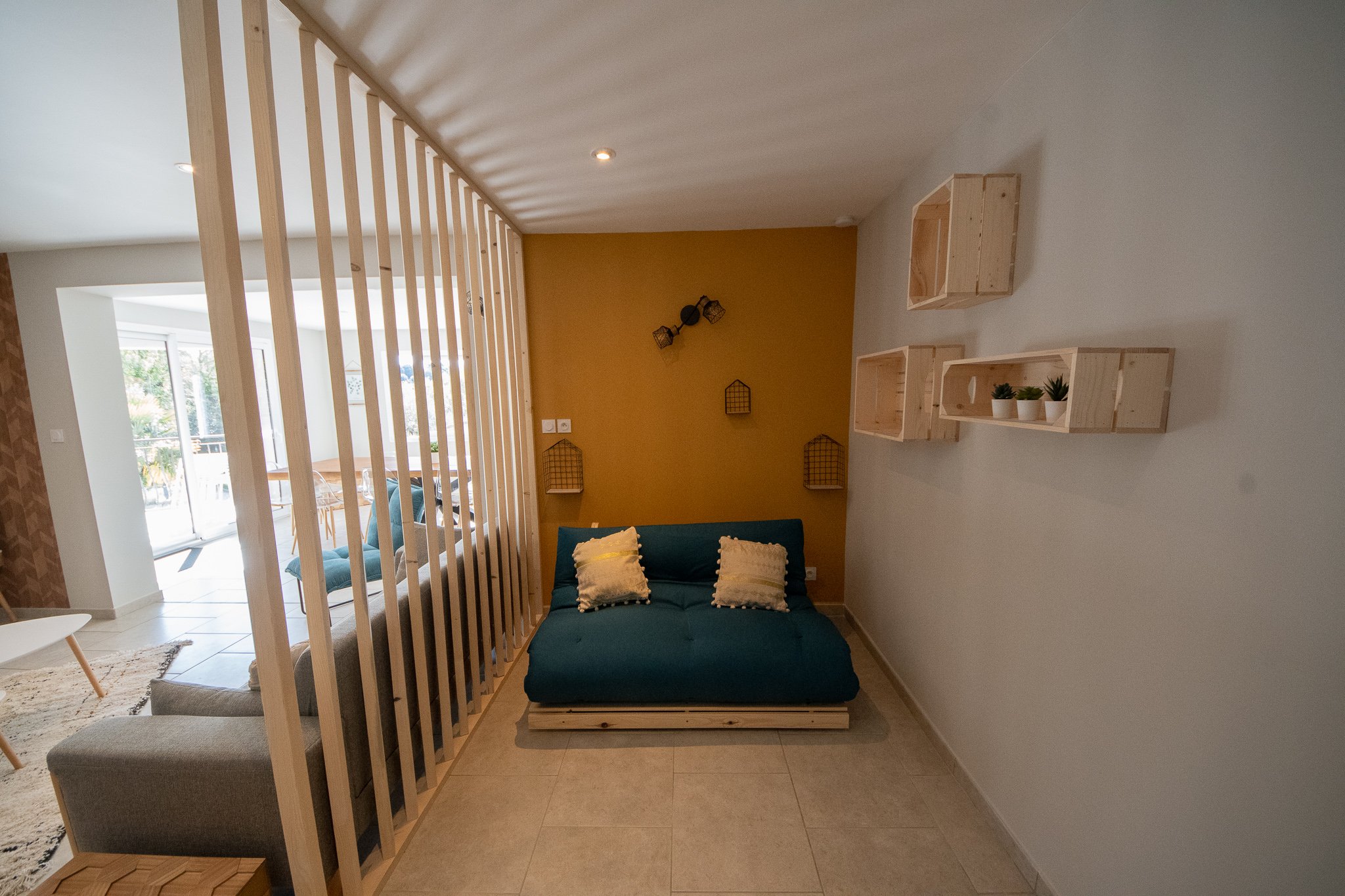 Salon avec canapé bleu, bibliothèque en bois sur le mur, mur beige, pièce lumineuse avec porte-fenêtre