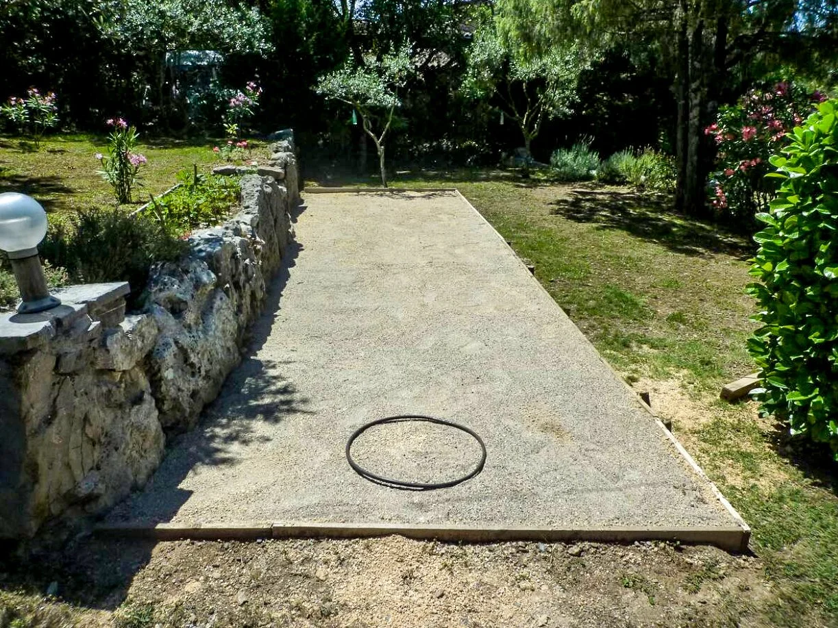 Un terrain de pétanque dans un jardin ensoleillé, entouré de plantes et d'arbres.