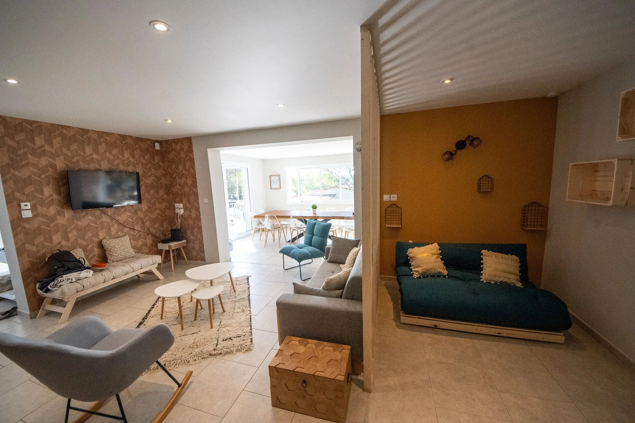 Salon ouvert avec des canapés, une télévision, une table basse, et une vue vers une salle à manger avec grande fenêtre.