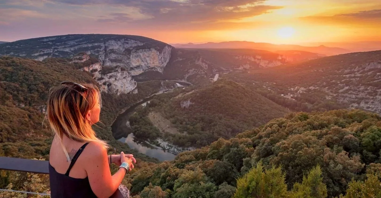 Femme regardant un paysage naturel avec une rivière, point de vue serre de tourre, des collines et un coucher de soleil.