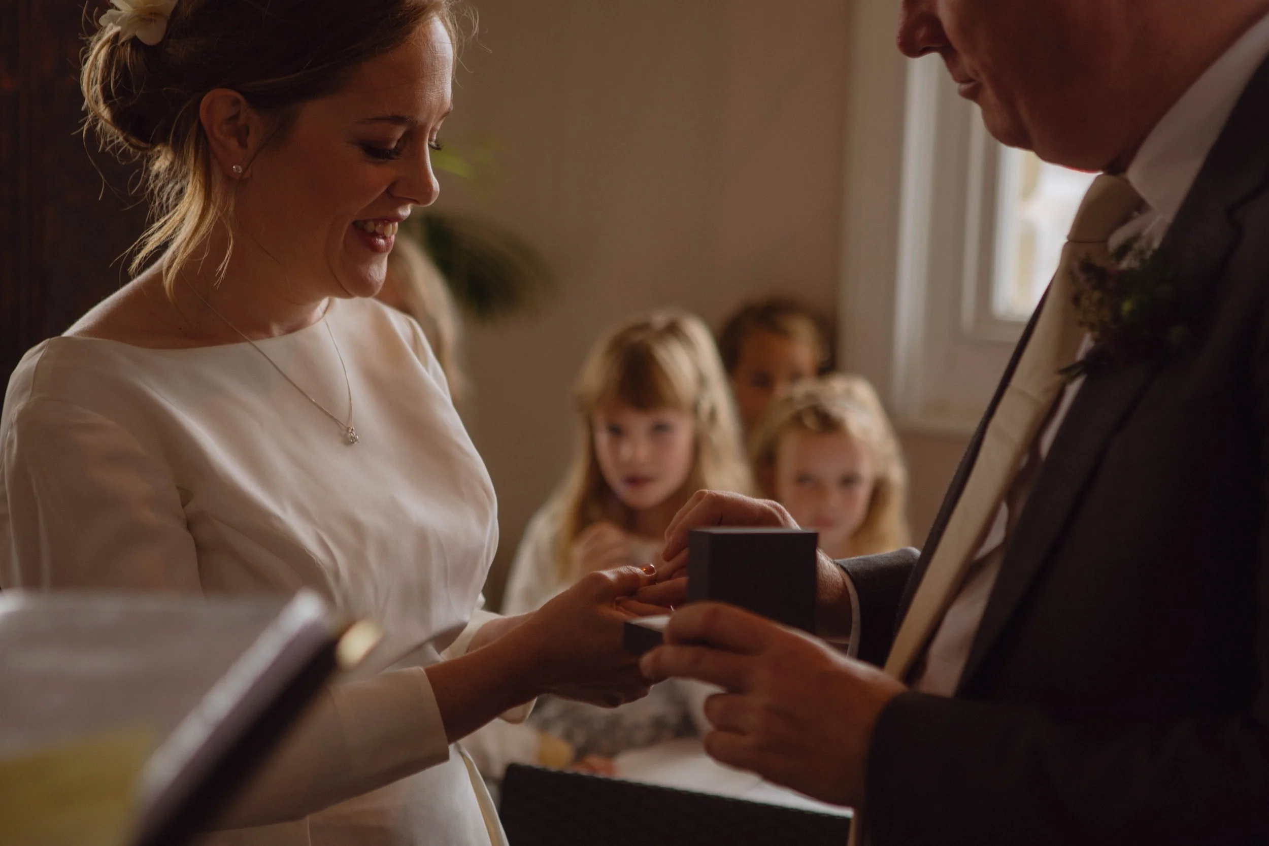 A woman receiving a ring box from a man during a wedding ceremony, with children in the background watching.