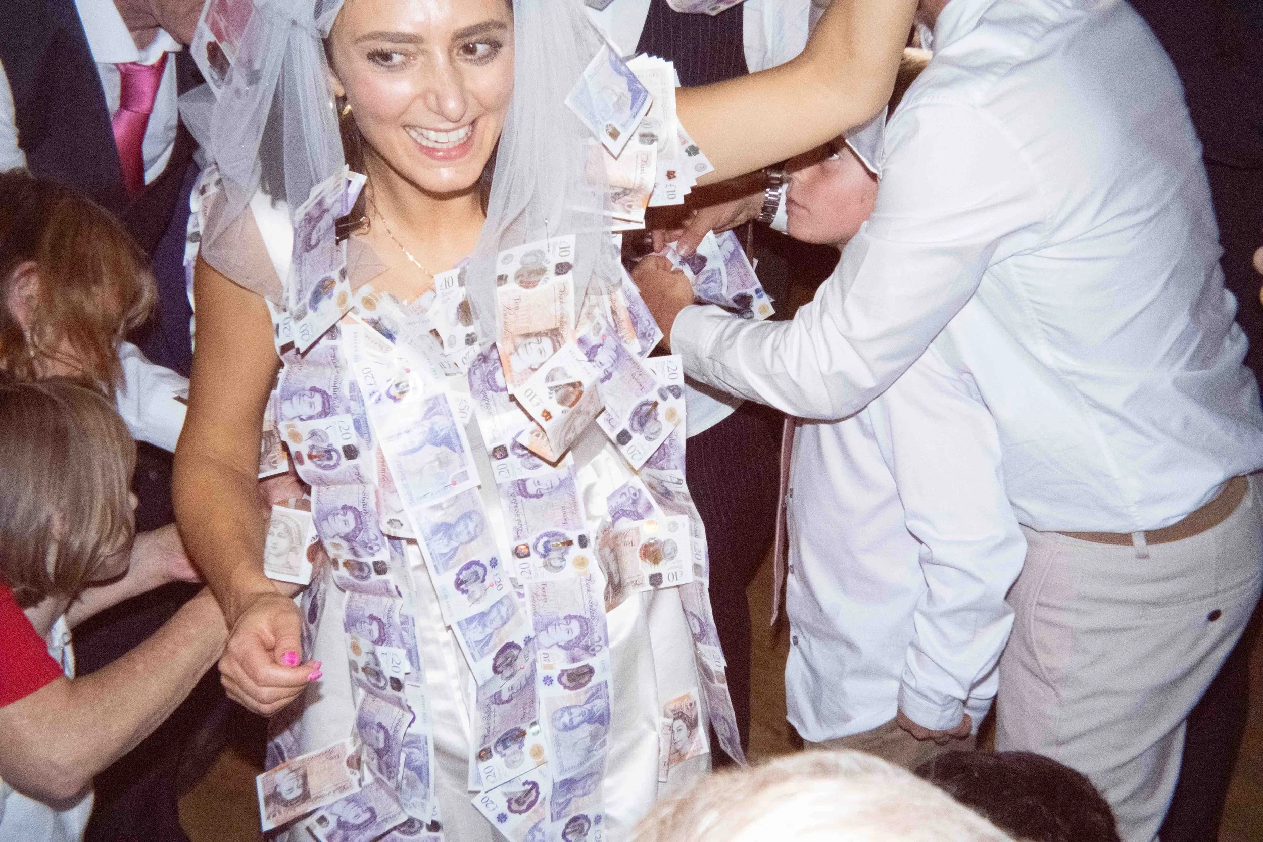 A woman in wedding attire covered with paper currency at a celebration event.