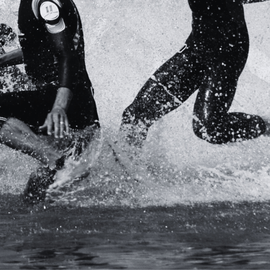 Two triathletes in wetsuits splashing water during a triathlon start.