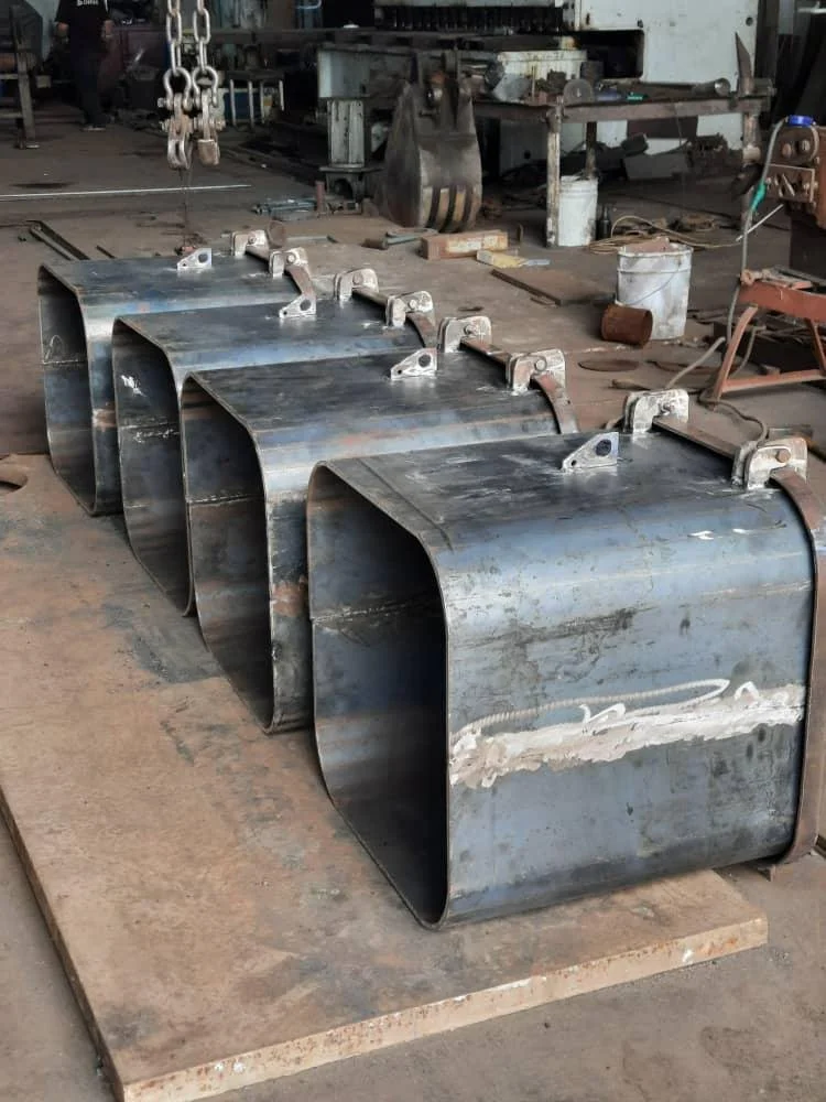 Four large, cylindrical metal pipe sections with flanges, arranged in a row on a workbench inside a workshop or factory setting.