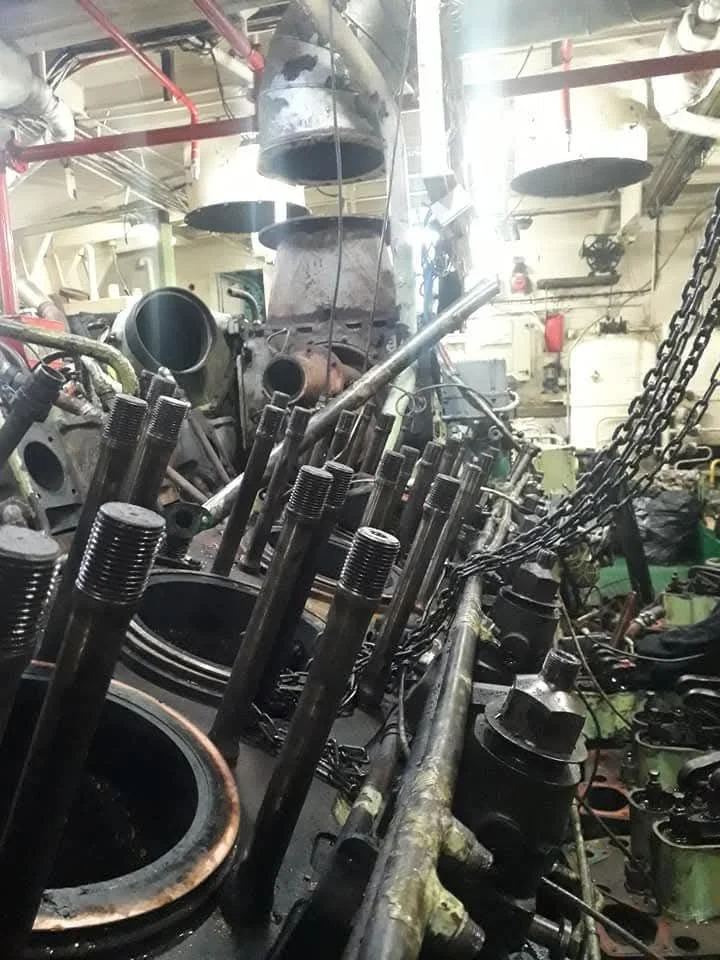 Disassembled large diesel engine with pistons, cylinders, and chains in an industrial workshop.