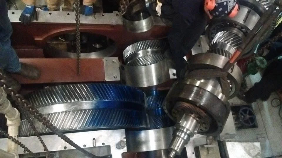 Heavy machinery with large metal gears and a long shaft in a workshop or factory setting.