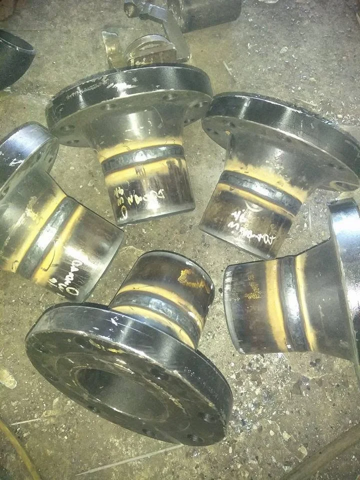 Six large metal cylindrical parts with a black and yellow coating, lying on a concrete floor. Some parts have writing on them.