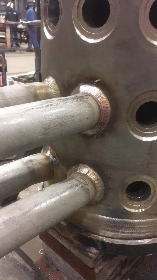 Four metal pipes welded to a large circular metal plate with multiple holes.
