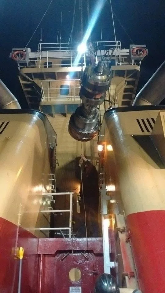 View looking up at a large ship's radar or antenna system at night, with bright lights and a person in the background.