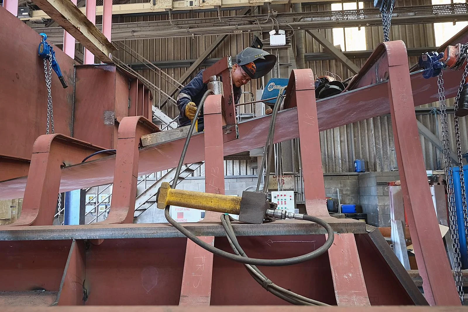 A worker welding metal beams inside a factory or workshop.