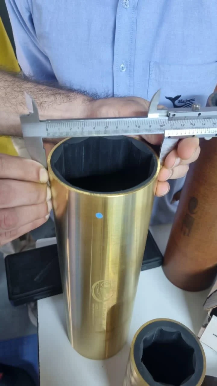 Person measuring the diameter of a large, gold-colored cylindrical object with a caliper.