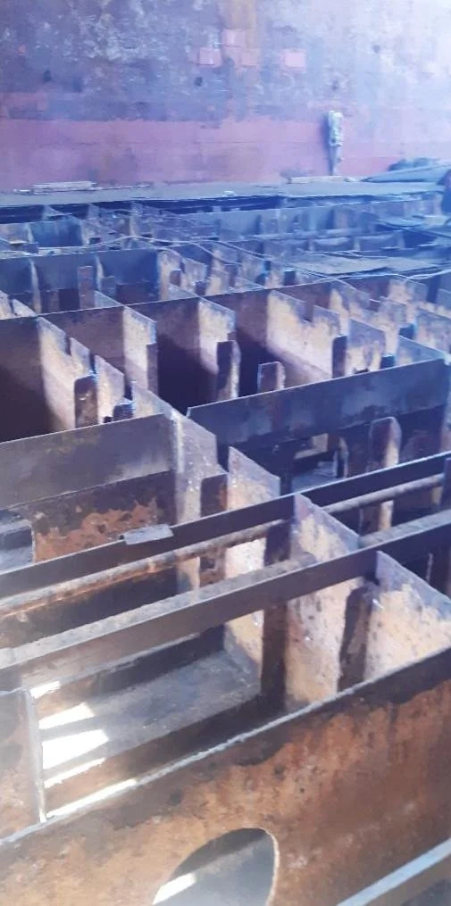 Close-up of rusted metal industrial equipment or structural components, possibly part of an old boiler or furnace, with a brick or concrete wall in the background.