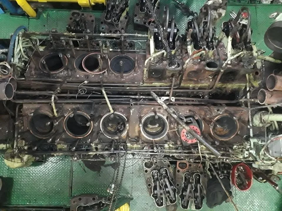 Disassembled car engine with various metal parts, pistons, and tools on a green work surface.