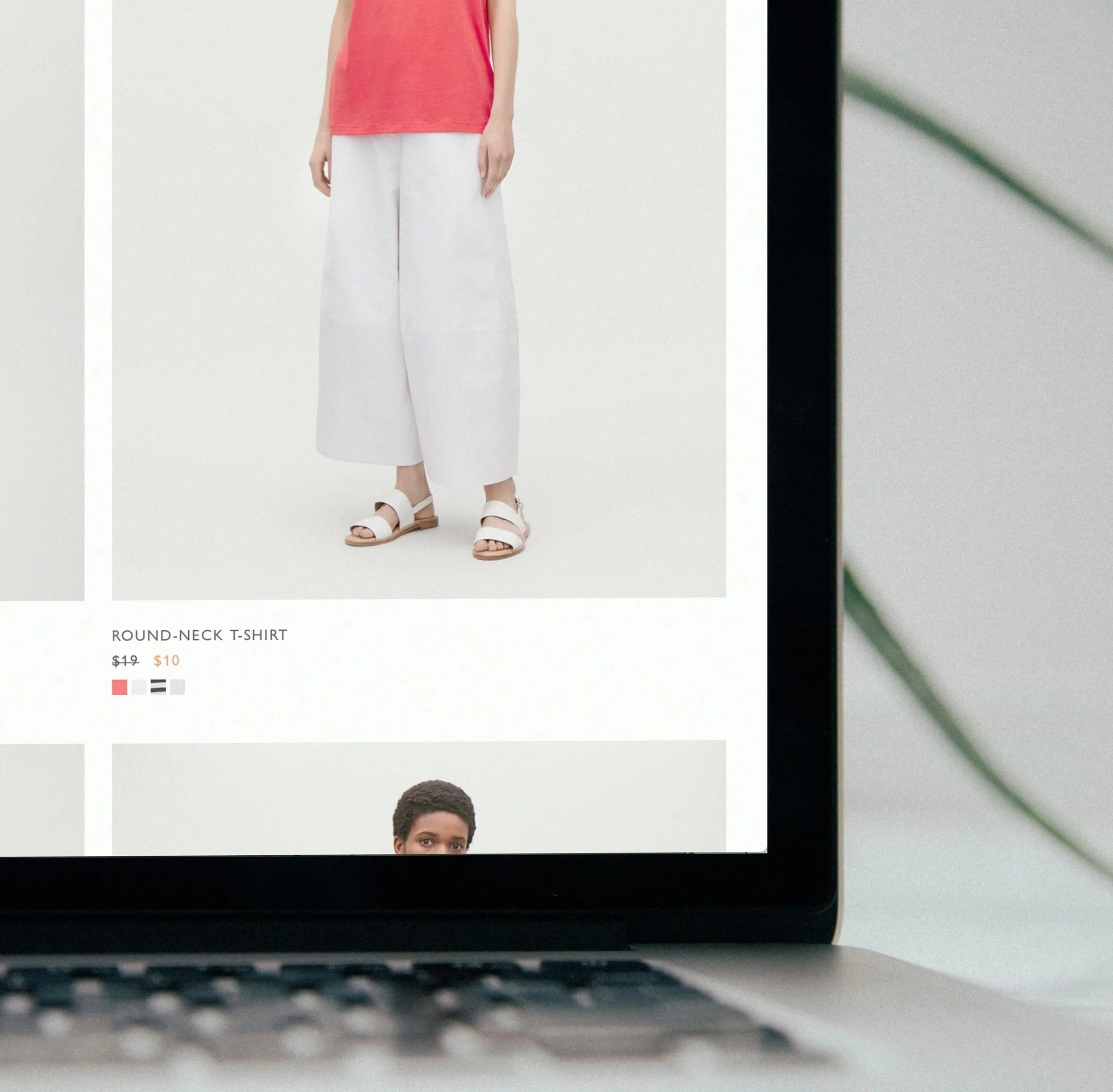 Laptop screen displaying an online clothing store with a model wearing a red t-shirt, white wide-leg pants, and white sandals.