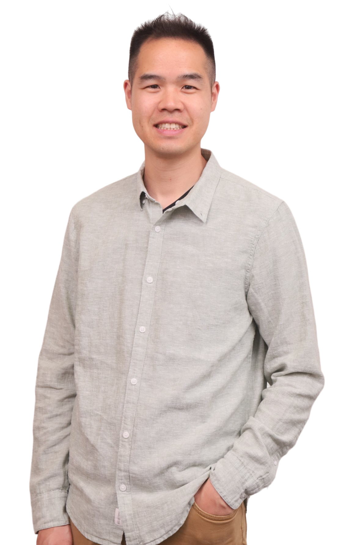 The founder of Oasis of Hope Psychotherapy, Calvin Lam, with short black hair smiling, wearing a light gray button-up shirt and tan pants, standing with one hand in his pocket.