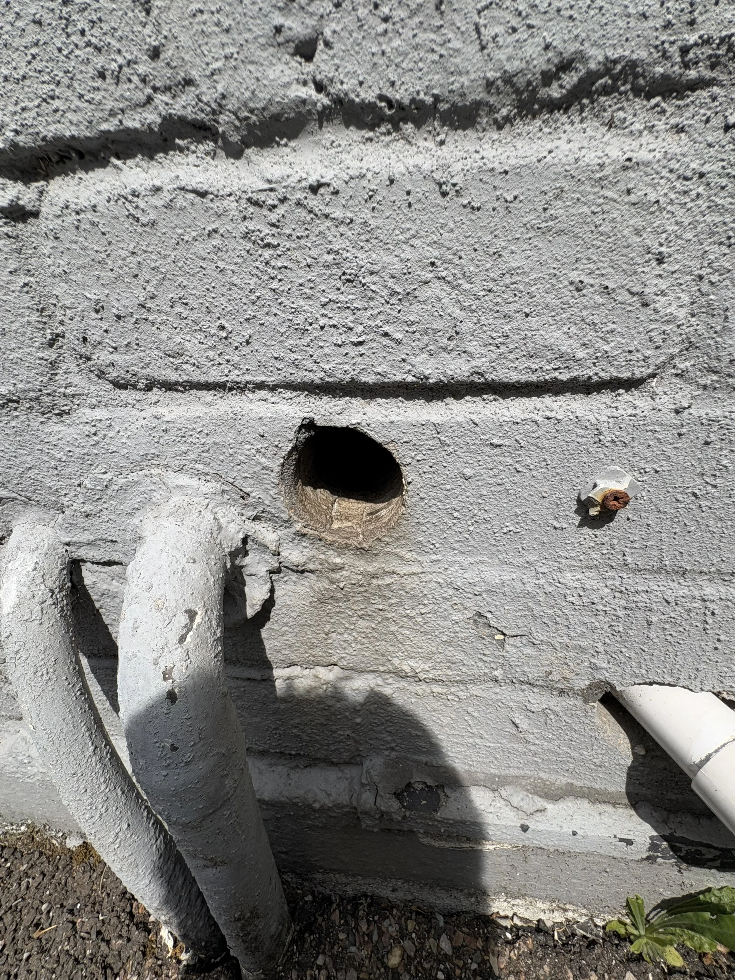 Close-up of a concrete wall with a pipe opening and a rusty bolt.