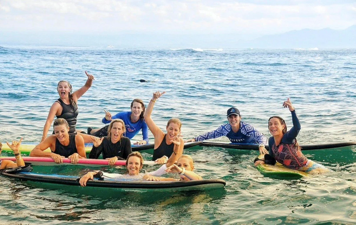 Group of women in life jackets on paddleboards in the ocean, smiling and posing for the camera.
