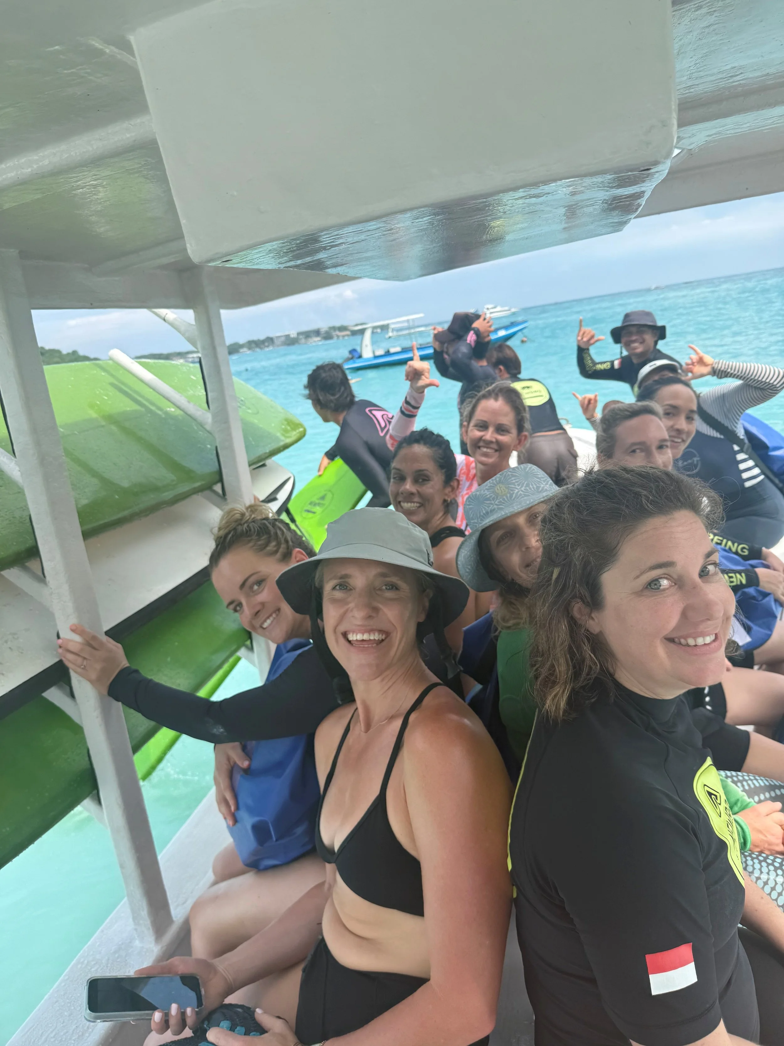 A group of smiling people on a boat, ready for a water activity, with the ocean and boats in the background.