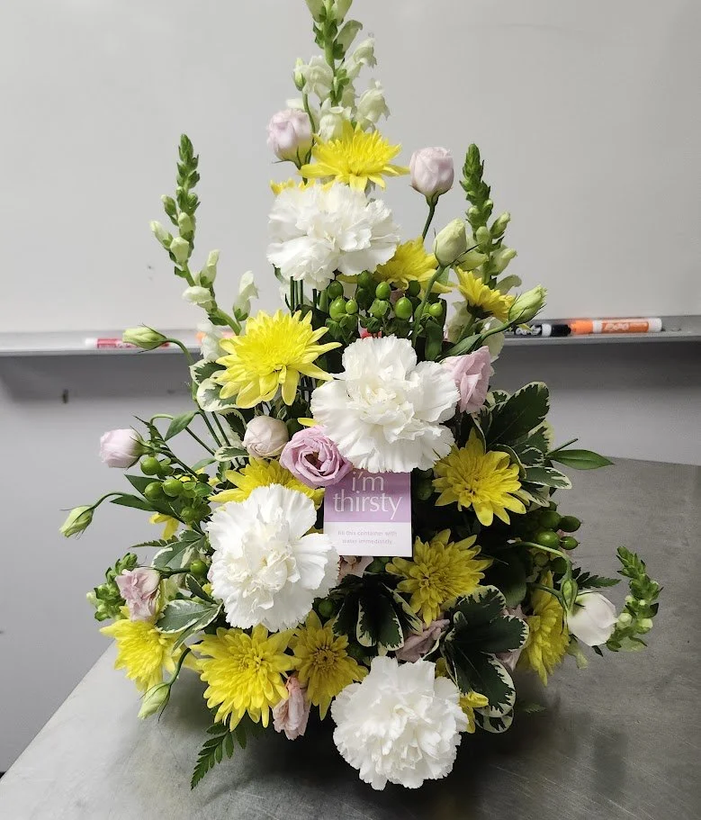 A tall arrangement with white carnations, yellow chrysanthemums, pink lisianthus, and green hypericum berries