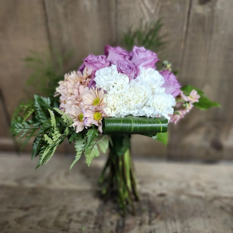A bouquet of pink roses, white carnations, and pink daisies with greenery