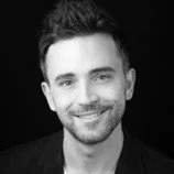 Black-and-white photo of a smiling man with short dark hair and a beard