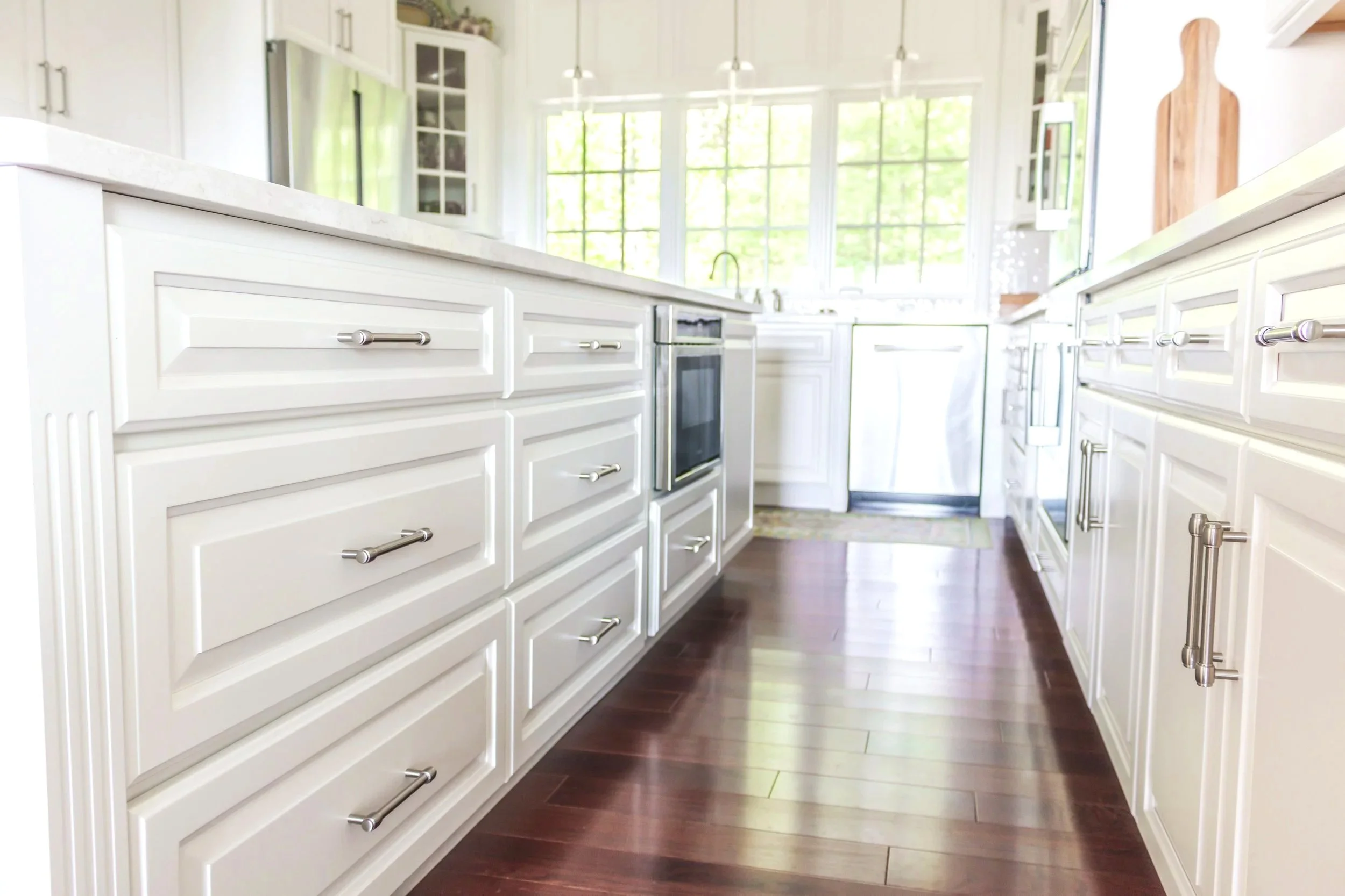 A man kneeling on the floor installing a cabinet door with a cordless drill in a kitchen. He is using a measuring tool to ensure proper alignment.