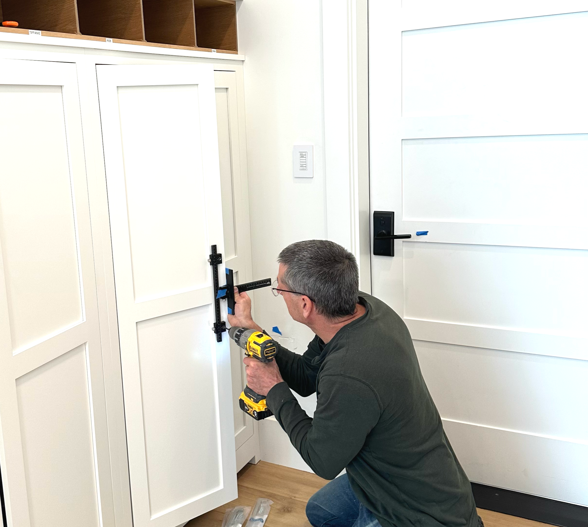 Person using a circular saw to cut a piece of trim on a large white and wood-colored cabinet in a home construction or renovation site.