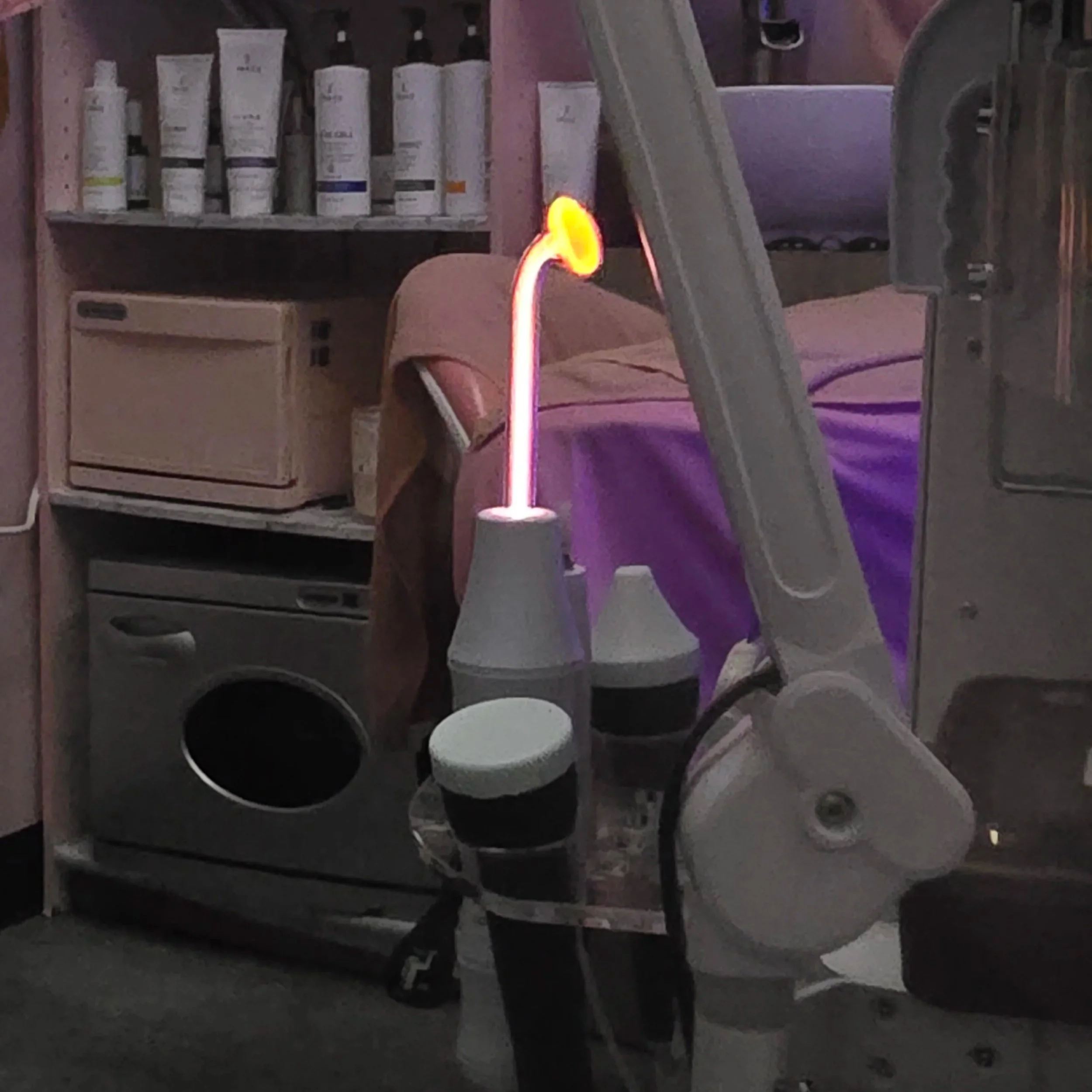 A multi-functional facial treatment machine with a glowing red light from a high frequency wand.