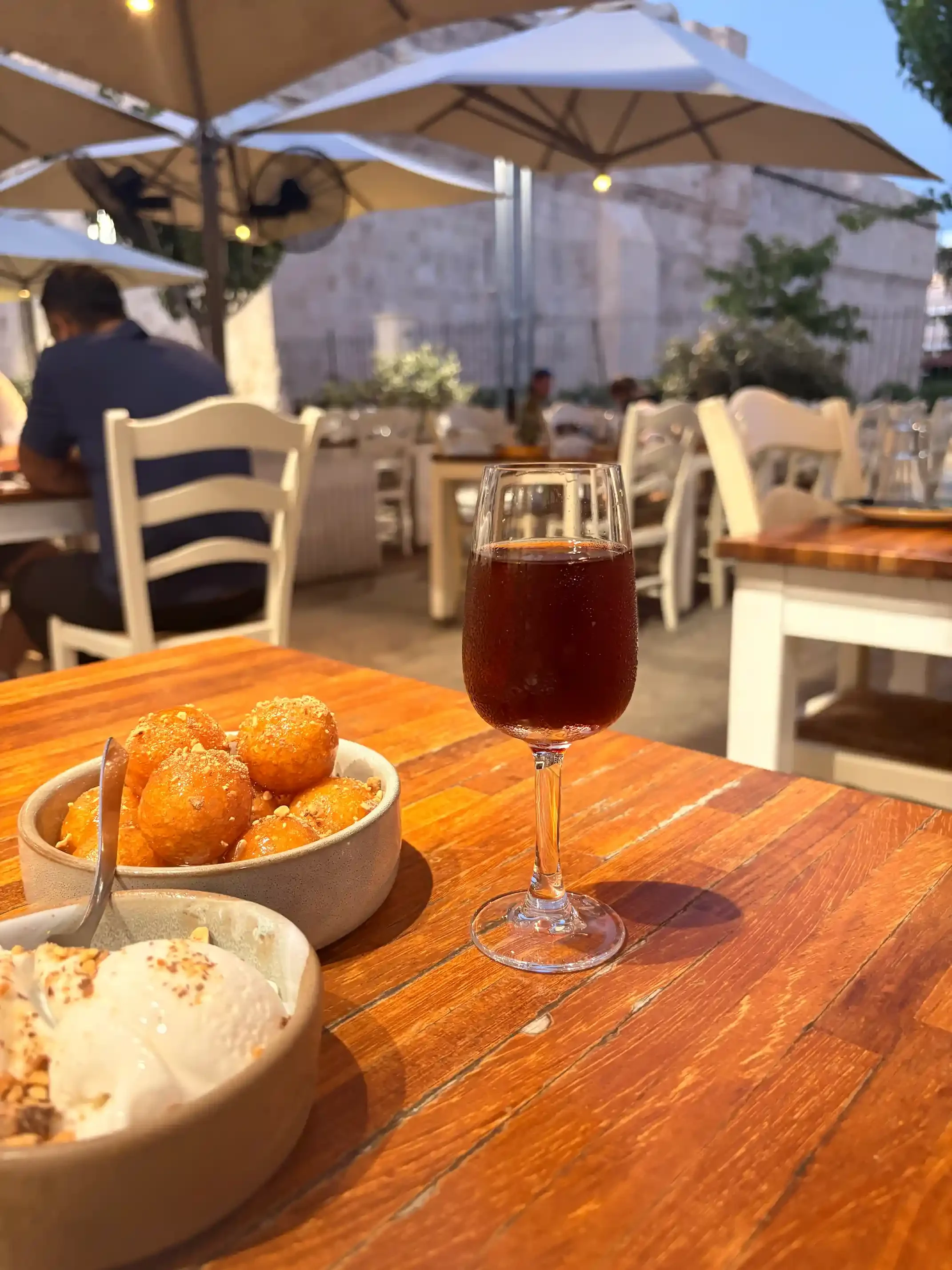 Loukoumades et glace dans des bols, avec un verre de commandaria, sur une table en bois en terrasse à Limassol