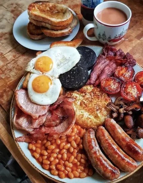 Full Scottish breakfast avec œufs frits, black pudding, bacon, saucisse, tomate, champignons et tasse de thé