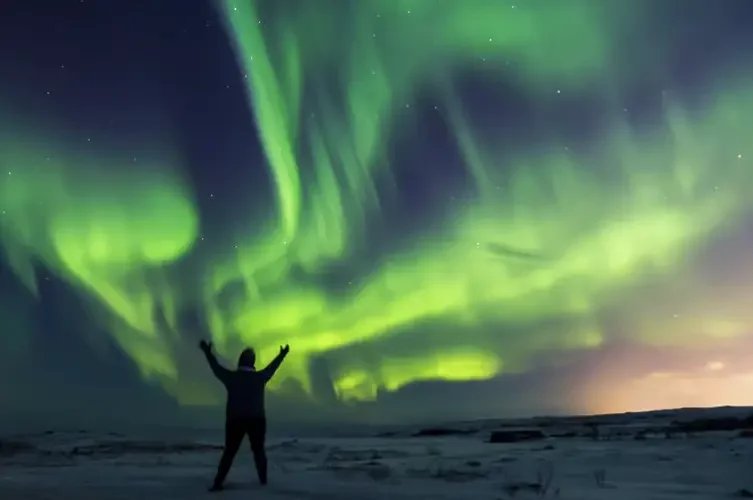 Aurore boréale verte dans le ciel islandais, avec un touriste surexcité au premier plan