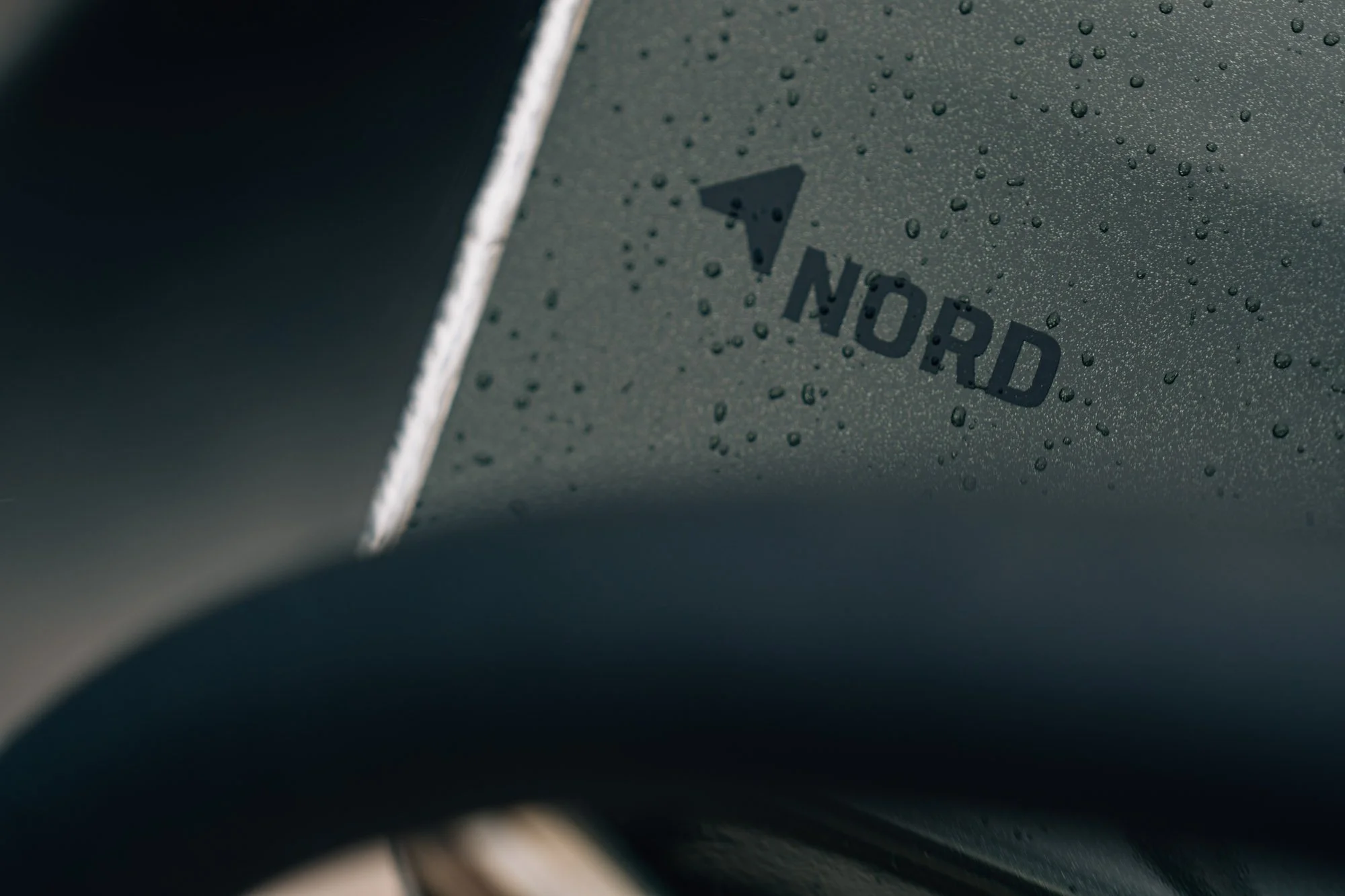 Close-up van een auto met waterdruppels op het oppervlak, met het woord 'NORD' en een pijl erop