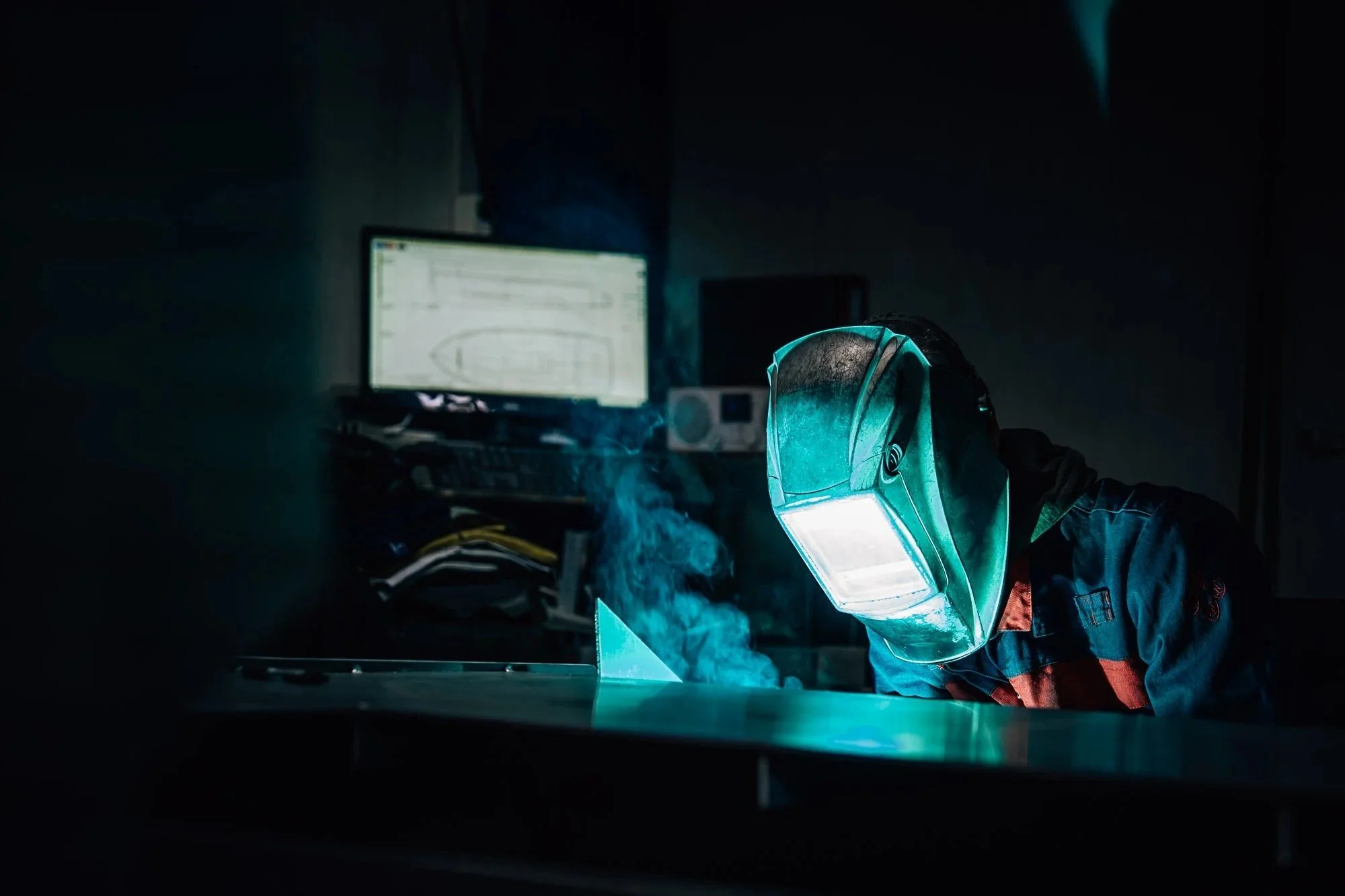 Persoon in een masker die in een donkere kamer werkt, met een computerscherm met de Nord 6, en rook op de achtergrond.