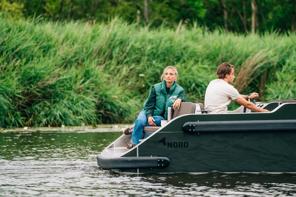 Een vrouw en man ontspannen op een boot op een meer met groen omliggend landschap.