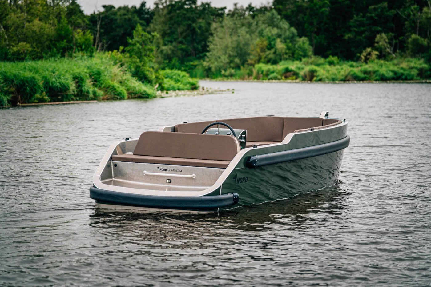 Een houten boot met bruine zitplaatsen drijft op een rivier, omgeven door groen struikgewas en bomen.