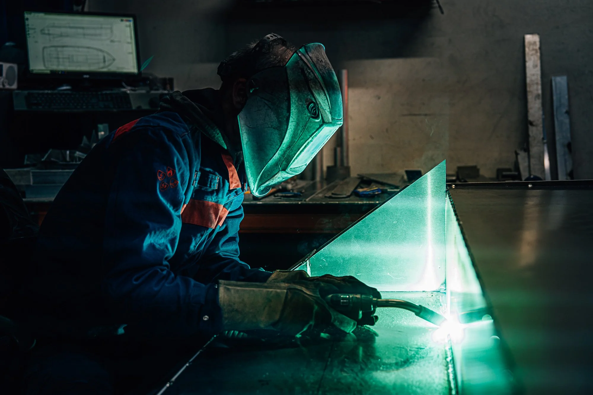 Een lasmonteur van lasbedrijf Leeuwarden die een metalen plaat las in een werkplaats, met een veiligheidshelm en handschoenen.