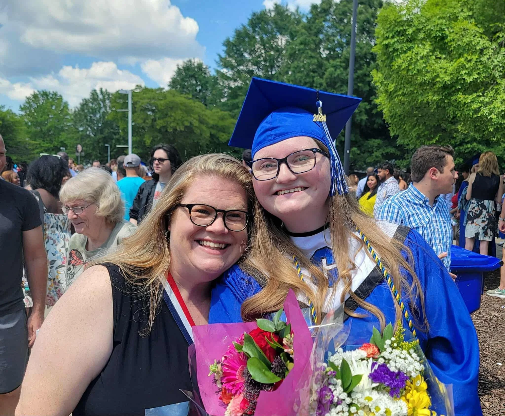 A young women in a high school graduation gown is standing with her mother, holding a diploma.