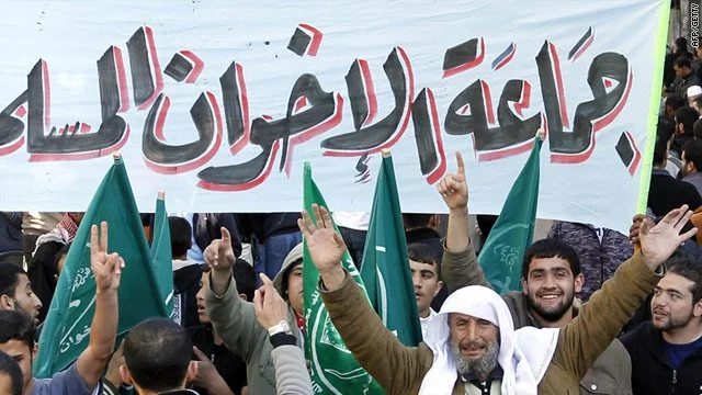 A group of people protesting with flags of Muslim Brotherhood and a large banner with Arabic writing.