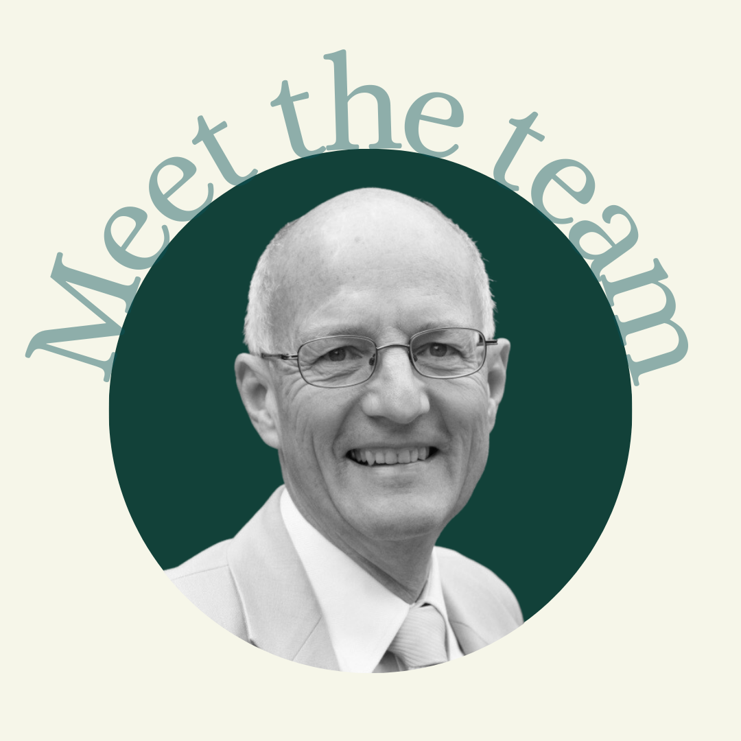 A grayscale photo of a smiling man with glasses, a bald head, wearing a suit and tie, with the words 'May the team' in a curved text above his head.