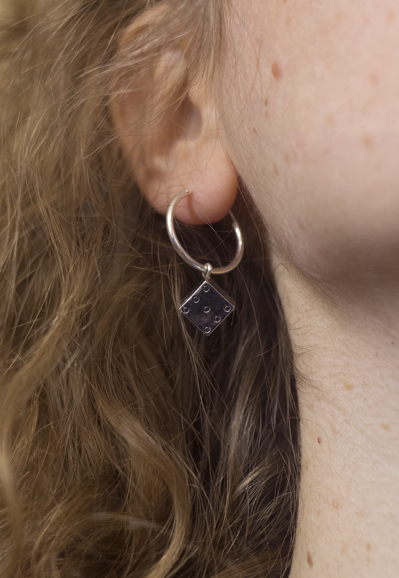 Close-up of a woman's ear with a silver hoop earring that has a black die charm hanging from it.