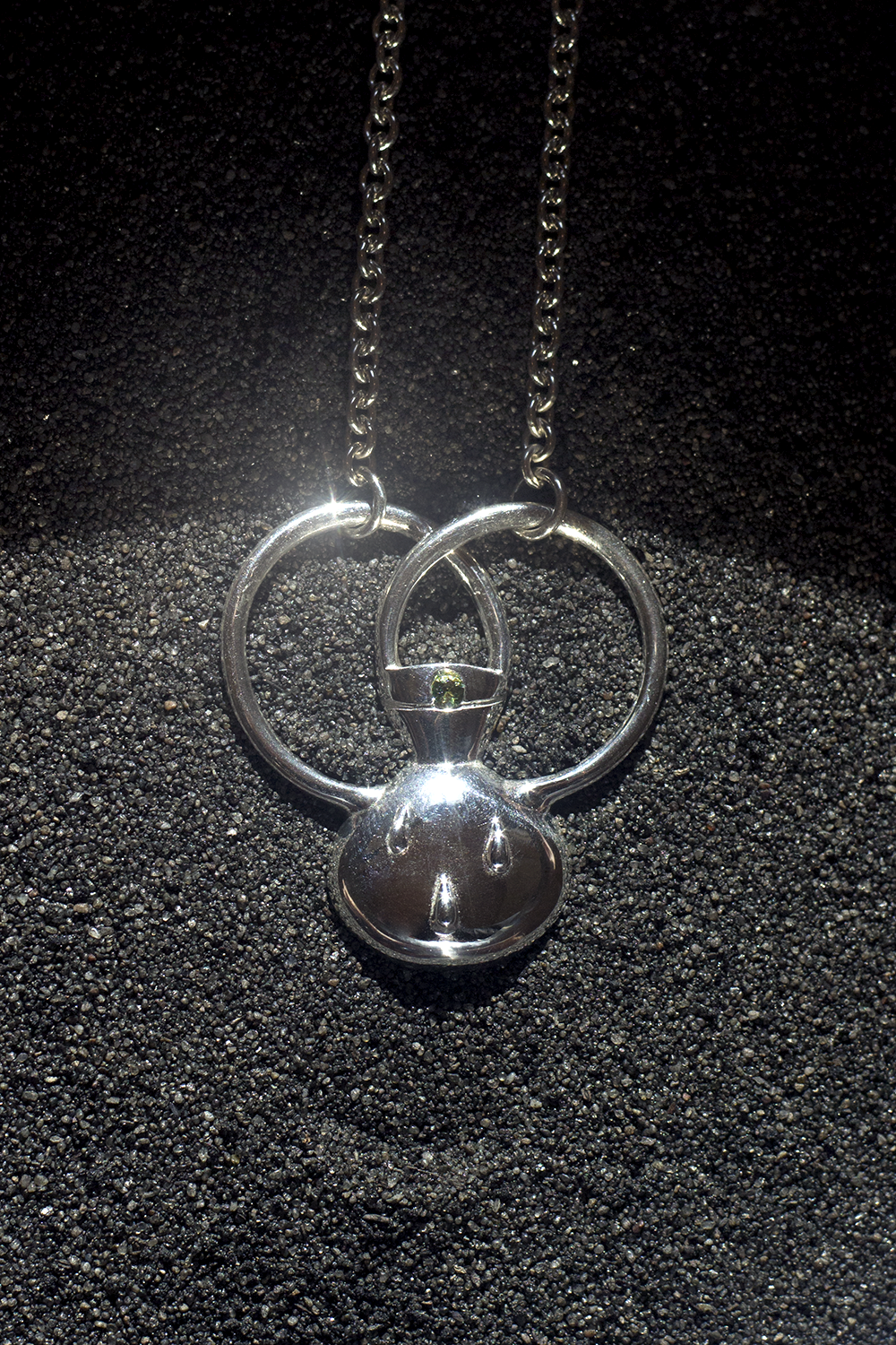 A silver necklace with a pendant shaped like Mickey Mouse's head and ears, with a small gemstone in the center, resting on black textured surface.