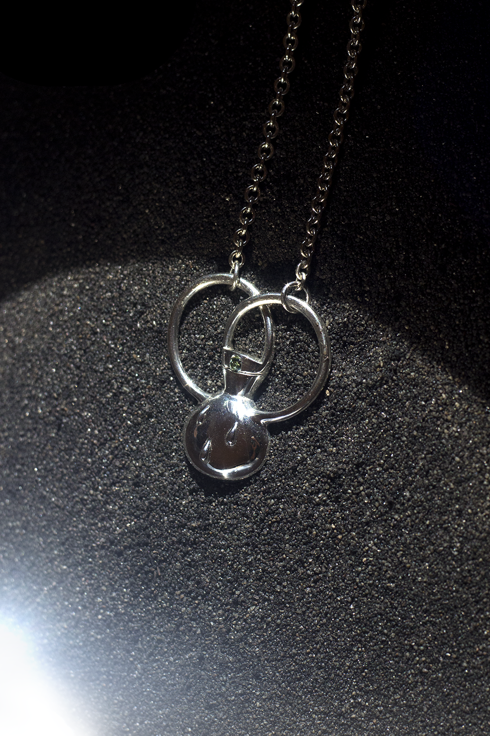 Silver necklace with a keychain pendant featuring a smiley face, resting on black textured surface.