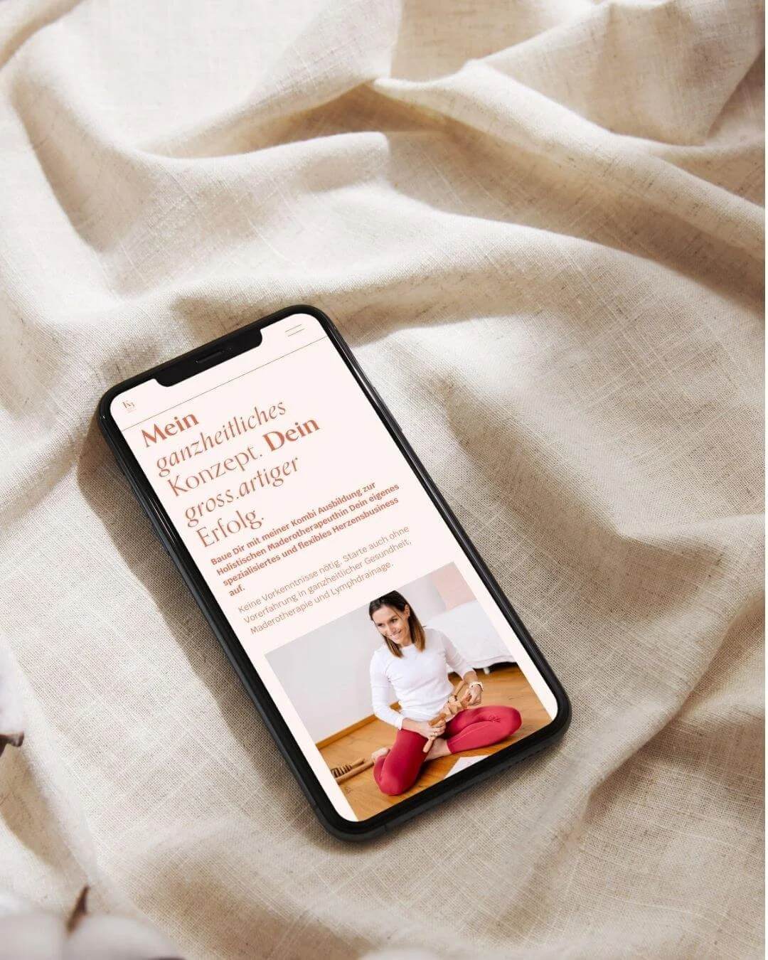 Smartphone auf beiger Stoffdecke, zeigt eine Website mit einem Bild einer Frau in Yogapose.