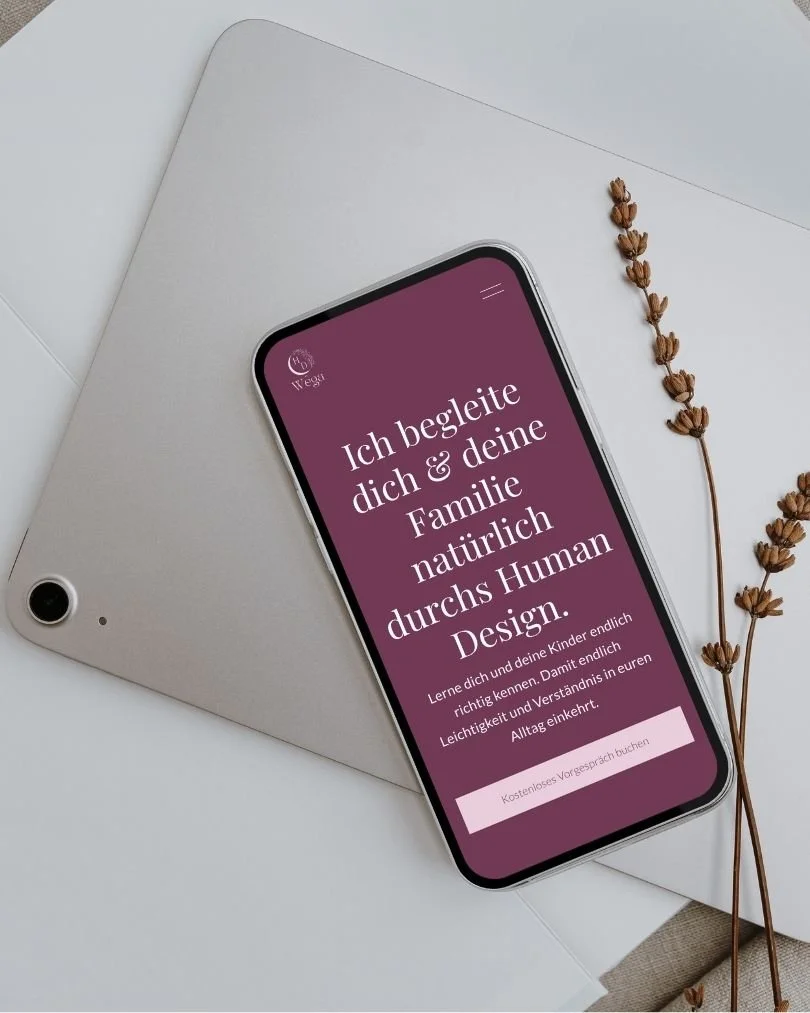Smartphone mit einem Text in Deutsch auf einem weißen Schreibtisch, neben einer Grafiks und trockenen Blumen.