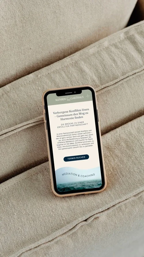 Smartphone auf einem grauen Sofa mit einer Webseite für Mediation und Coaching, die Konflikte löst und Partnerchaften verbindet.