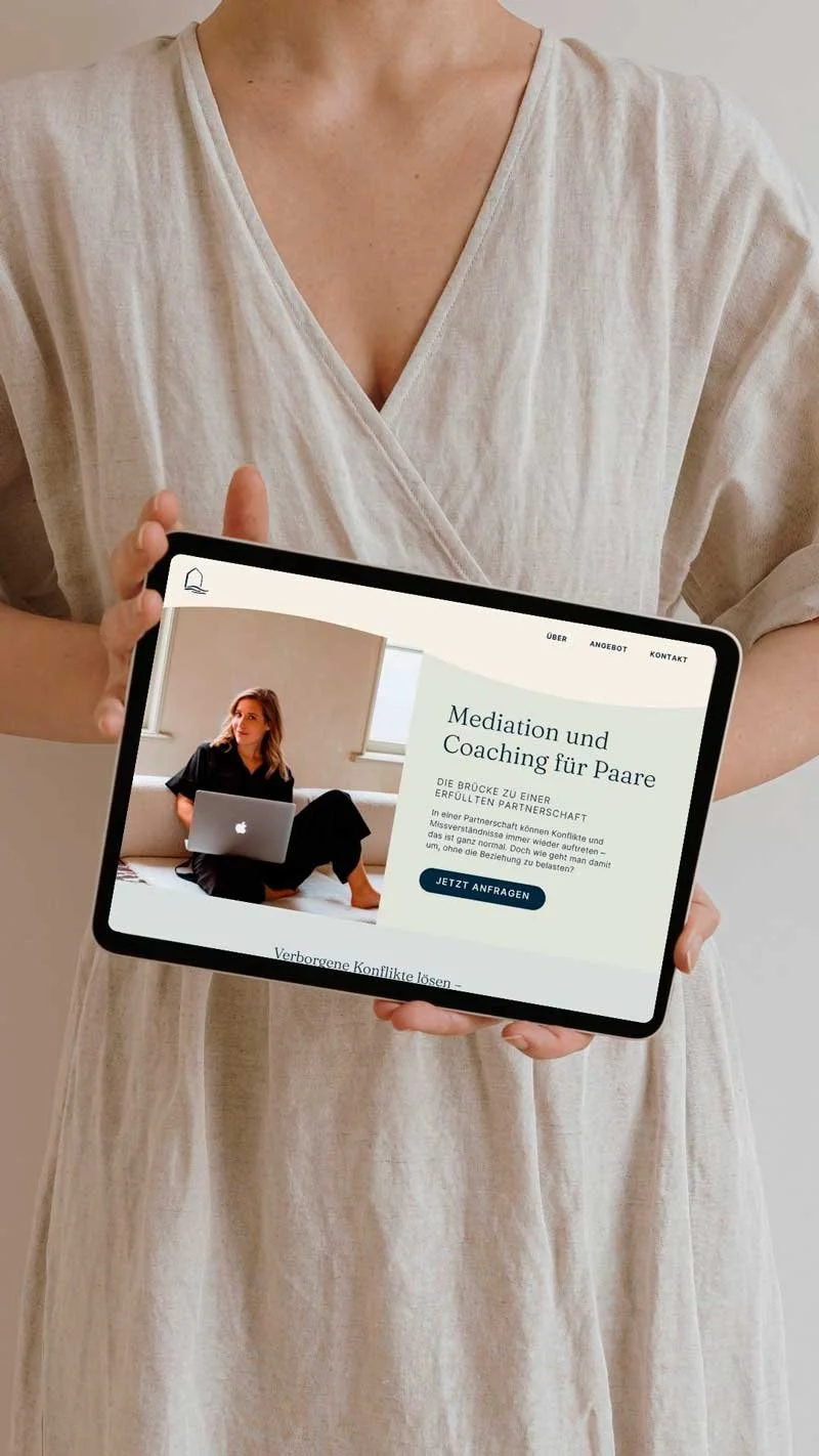 Eine Person hält ein Tablet mit einer Webseite über Paarmediation und Coaching, zeigt ein Bild einer Frau mit Laptop, im Hintergrund ein helles Zimmer.