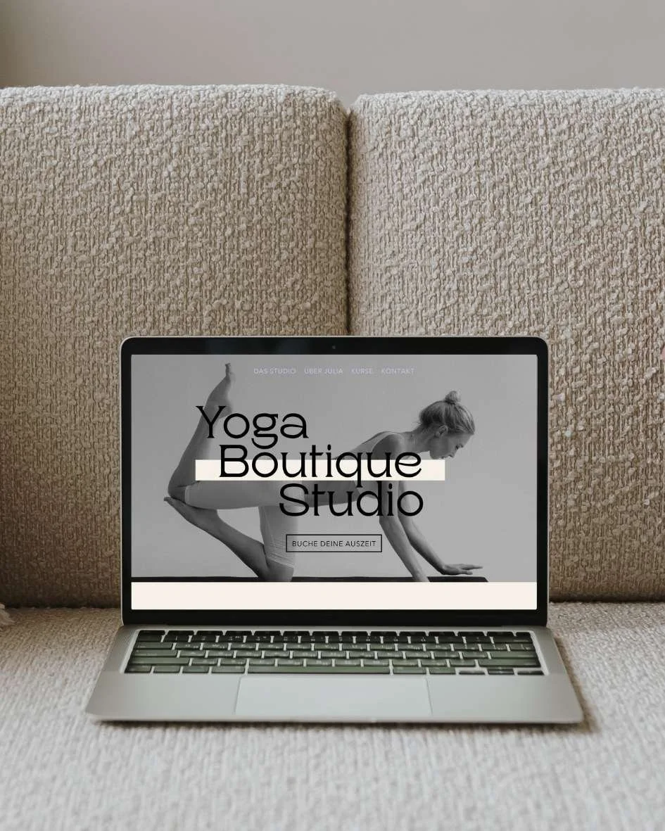 Laptop auf einem Sofa zeigt Webseite eines Yoga Studios, in Schwarz-Weiß-Bild einer Frau im Yoga, Text "Yoga Boutique Studio" und Button "Buche deine Auszeit"