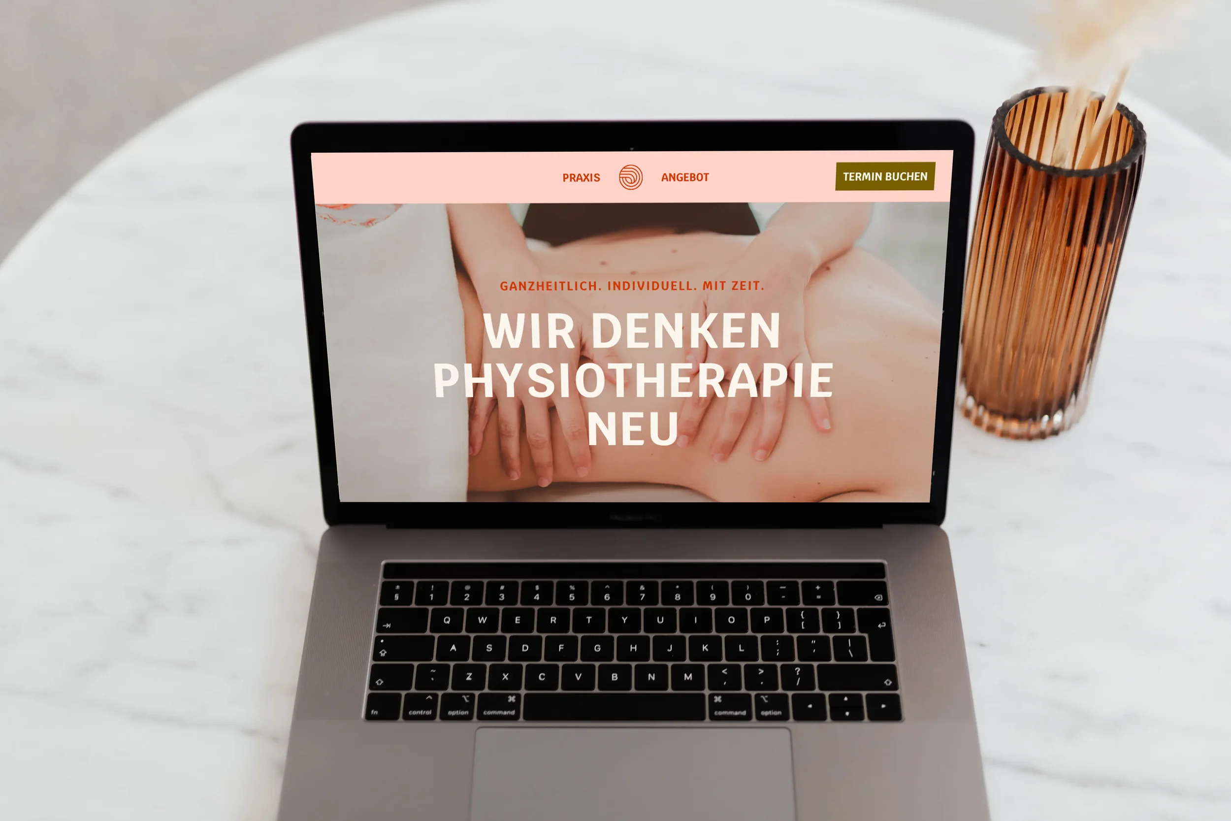 Laptop auf einem weißen runden Tisch mit einer Webseite zur Physiotherapie, neben einem braunen Holzstifthalter.
