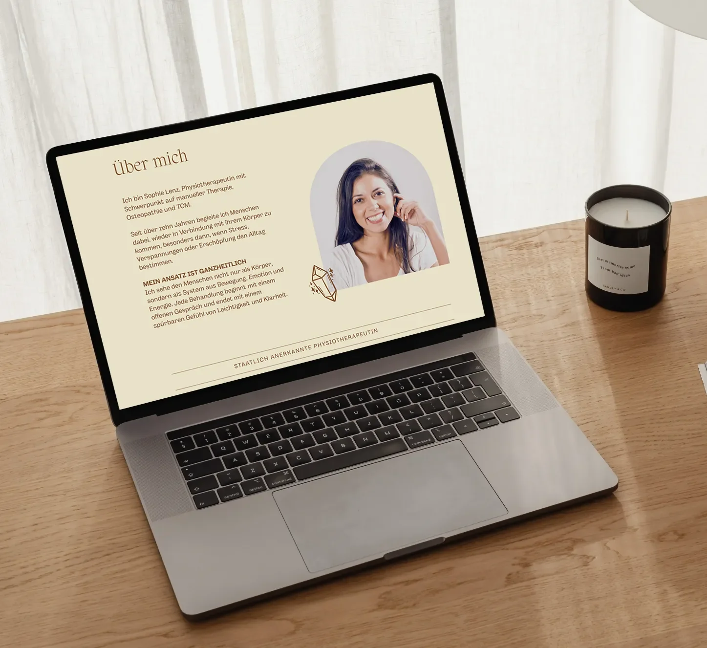Laptop zeigt eine Webseite mit einer Vorstellung einer Physio-therapeutin, neben einem schwarzen Kerzenglas auf einem Holztisch.