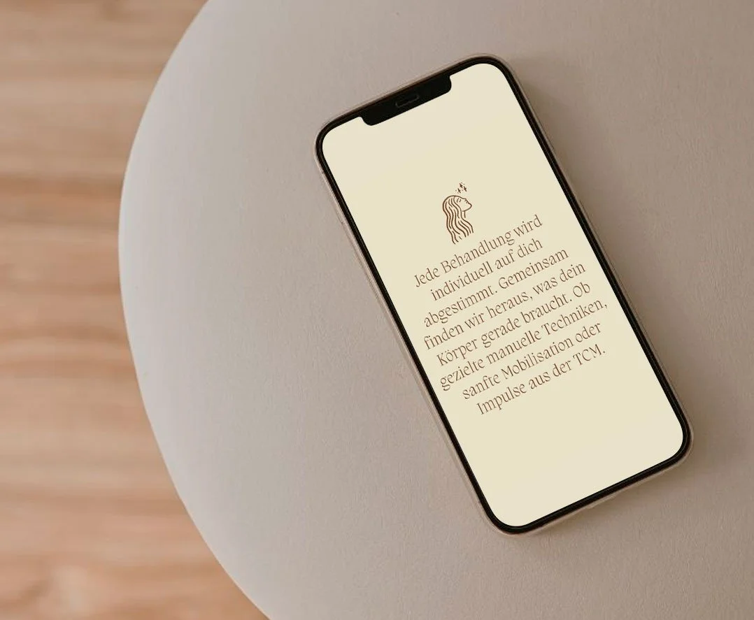 Smartphone liegt auf einem runden weißen Tisch, zeigt eine Webseite mit Infos zu individuellen Behandlungstechniken, symbolisiert durch eine Hafenauslippen-Illustration.